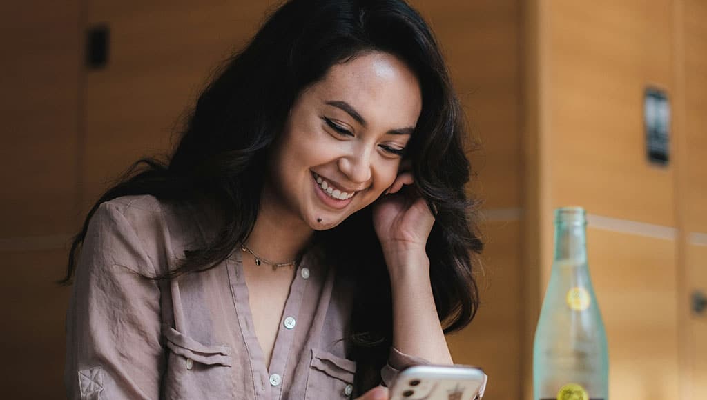 girl-sitting-at-table-looking-at-phone-1024×580